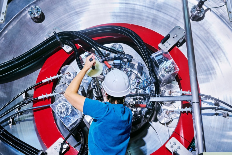 Pictured: An employee is seen working on TAE Technologies’ fusion energy research device at the company’s offices in Foothill Ranch, CA. TAE’s current fusion device, Norm, is the first machine designed to form field-reversed configuration (FRC) plasmas using only neutral beams. About 40 feet in length, Norm radically improves the cost and power efficiency of TAE’s proprietary advanced beam-driven FRC, which combines accelerator physics and plasma physics to solve the challenge of high-quality plasma confinement. TAE’s neutral particle beam technology forms a hollow football of superheated plasma right in the center of the Norm machine, where the plasma is confined by magnets and the plasma’s own magnetic field. The plasma is then rotated by eight particle beams that help heat and stabilize the superhot gas for fusion. Designed by an ambitious team of physicists, engineers, and technicians from around the world, Norm is optimized with cutting-edge power delivery and active feedback control systems, as well as machine learning and algorithms co-created with Google. The device is named for Dr. Norman Rostoker, the man who inspired the company’s quest for the ultimate form of carbon-free commercial energy: aneutronic hydrogen-boron fusion. Credit: Spencer Lowell/TAE Technologies