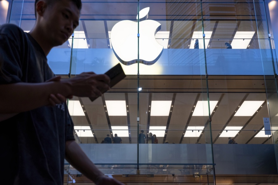 A pedestrian uses a smartphone while walking past an Apple store and logo in Hong Kong. (Image: Sebastian Ng/SOPA Images/LightRocket via Getty Images)