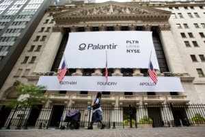 A mail carrier wearing a protective mask passes a banner displaying Palantir Technologies Inc. signage during the company's initial public offering (IPO) in front of the New York Stock Exchange (NYSE) in New York, U.S., on Wednesday, Sept. 30, 2020. Shares of Palantir Technologies, a data mining company co-founded by technology billionaire Peter Thiel, opened trading today on the New York Stock Exchange at $10 after the company sold shares to investors in a direct offering. Photographer: Michael Nagle/Bloomberg via Getty Images