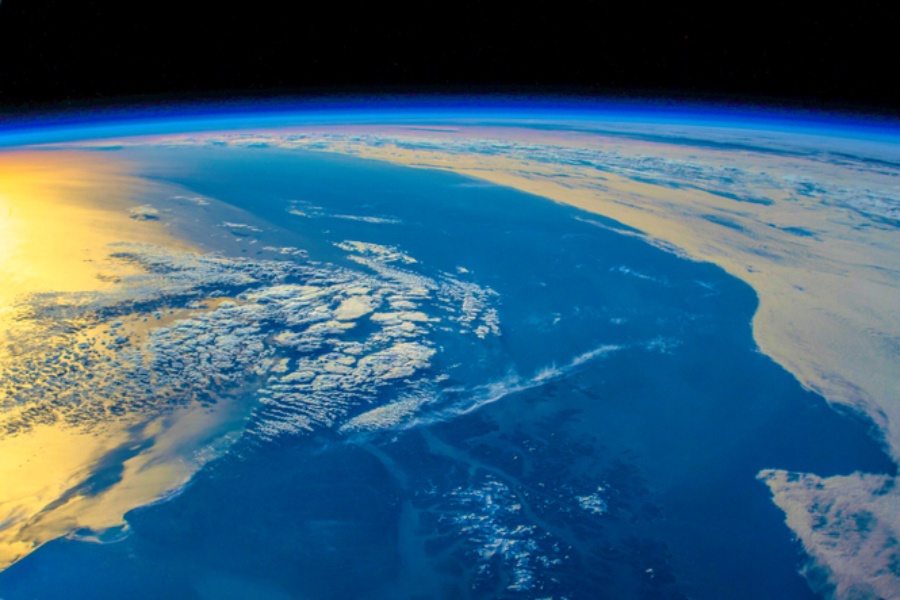 Sunlight intense reflections over the ocean. The horizon and atmosphere of our home planet. The saturation, vibrancy, and texture have been changed to enhance the beauty of our blue planet. Some small clouds over the yellow reflections have been added to create a trail-like line. The ISS was over the South part of Chili when the original image was taken. Elements of this image furnished by NASA