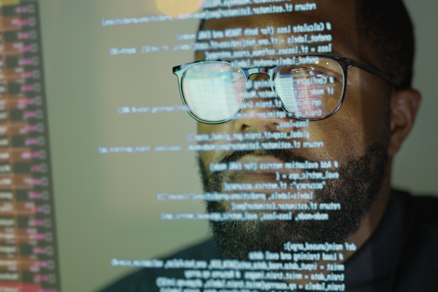 Stock photograph of an afro Caribbean (afro American) man studying a see through display depicting Python computer coding.